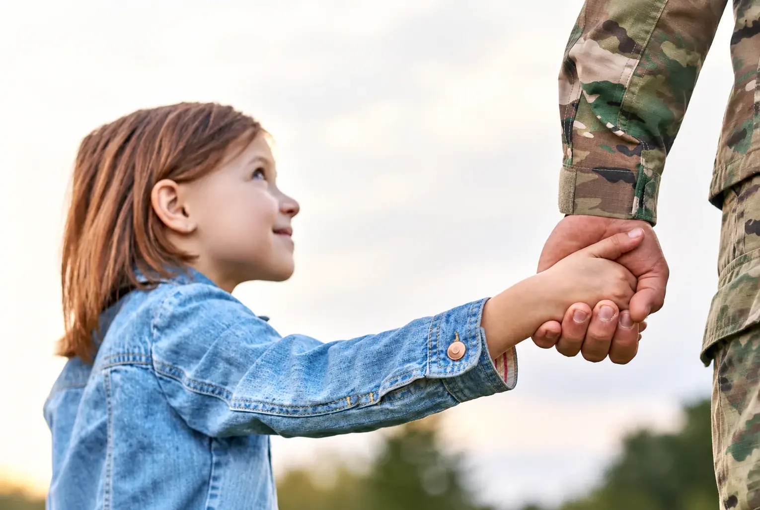 A young girl holds the hand of a uniformed service member