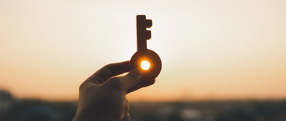 Hand holding a key with a sunset in the background.