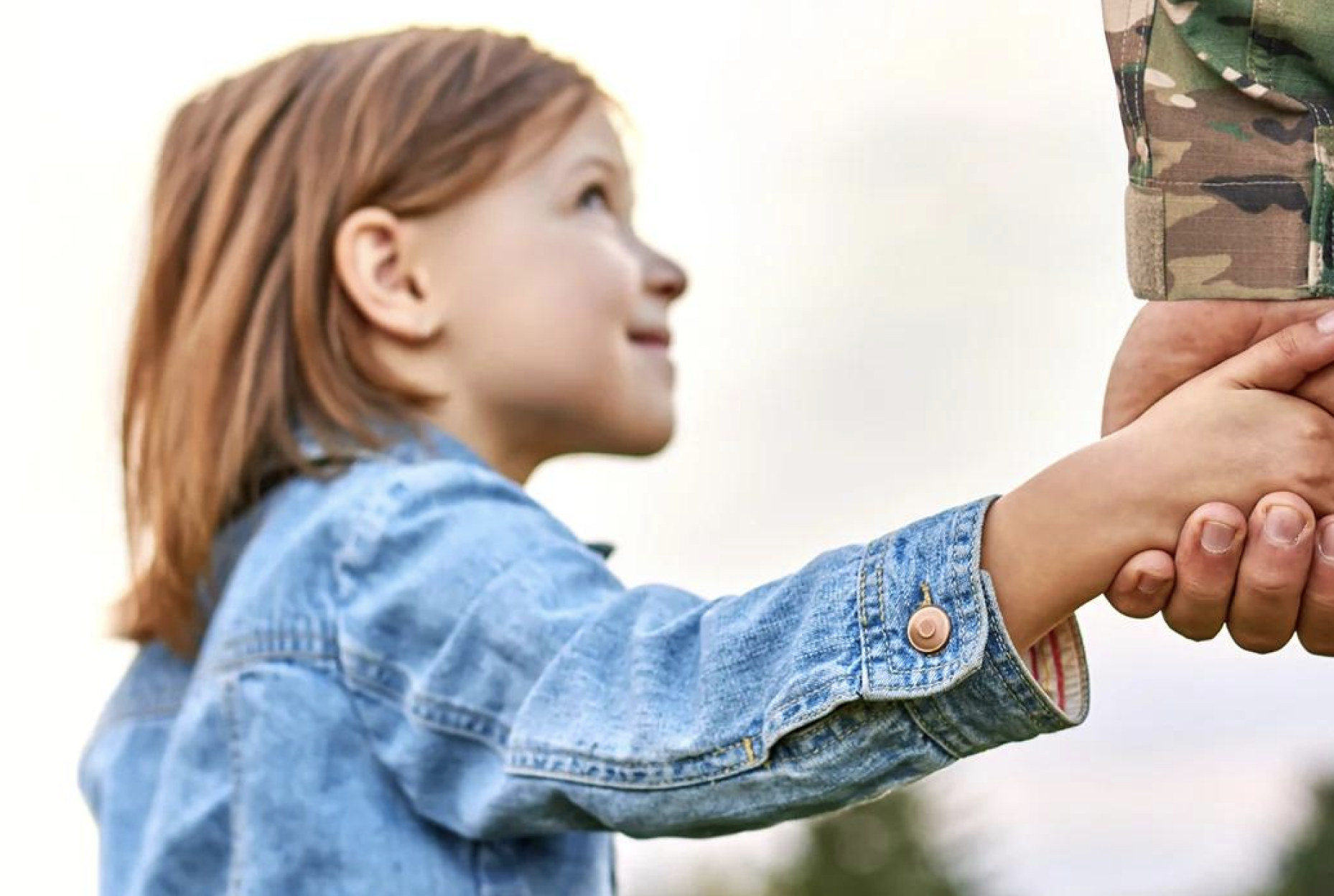 A child reaching out to take her military parent's hand
