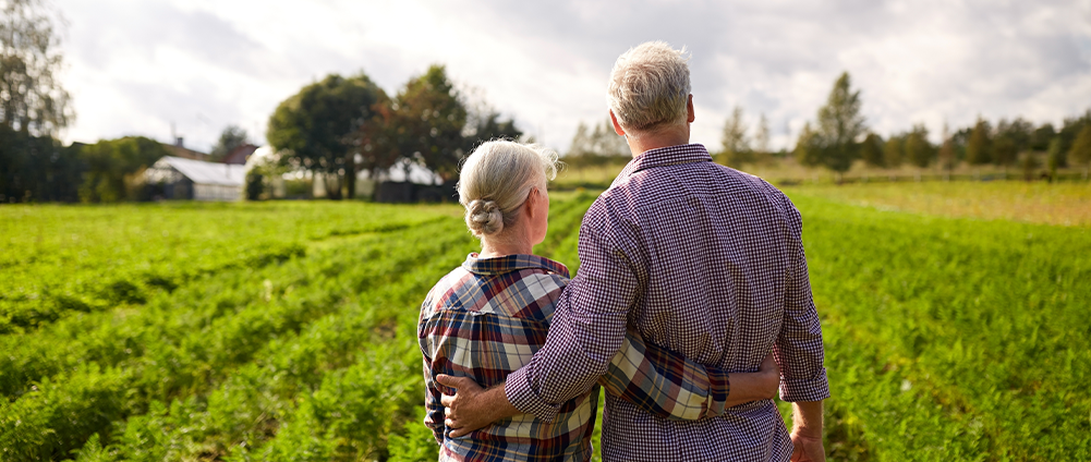Retired military couple with their arms around each other surveying their land.